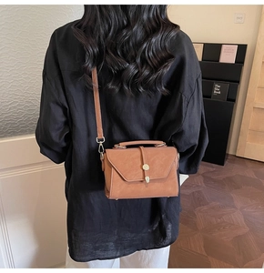 Detail of vintage brown crossbody bag with gold buckle worn by model in cozy library