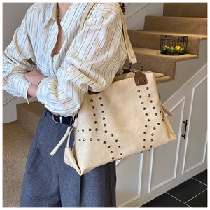 Close-up of beige tote bag with metallic rivet details and brown leather side reinforcement