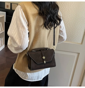 Detail of dark brown vintage crossbody bag with elegant gold metal buckle and pendant
