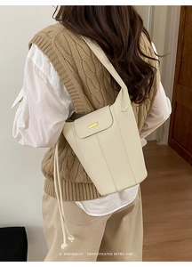 Sac seau minimaliste en cuir beige avec détails dorés porté par un mannequin