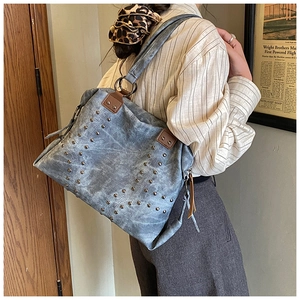Detail of blue denim tote bag with silver star-shaped rivets and brown leather strap accents