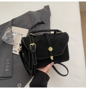 Detailed view of black matte leather handbag with white contrast stitching and gold buckle