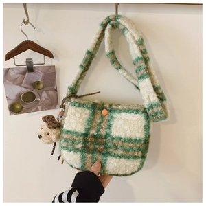 Close-up of green checkered plush shoulder bag with orange button and teddy bear charm
