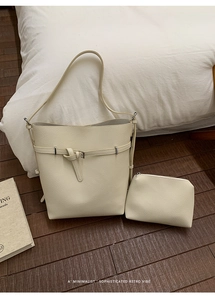 Detail view of beige lychee textured leather bucket bag set on a wooden floor