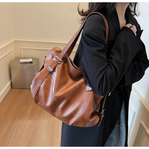 Détail d'un grand cabas en cuir marron avec boucles argentées porté par un mannequin