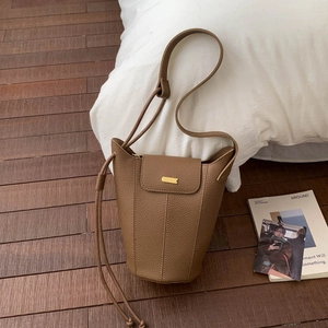 Détail du sac seau en cuir grainé marron avec finitions dorées sur parquet en bois