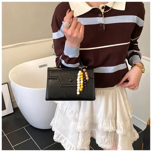 Detail of black matte leather handbag featuring a round buckle and beaded tassel charm