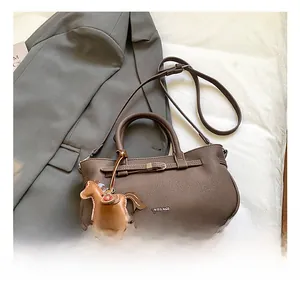 Detail of dark brown pebble leather handbag with horse charm on grey blazer