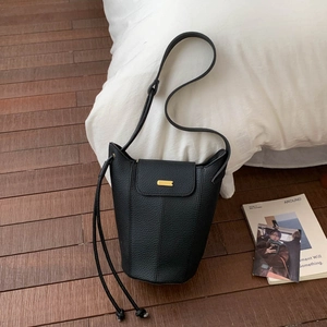 Détail du sac seau en cuir grainé noir avec boucle dorée sur un fond de bois sombre