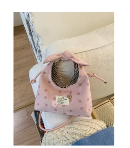 Detail of pink polka dot suede handbag featuring a bow handle and cartoon cat patch label