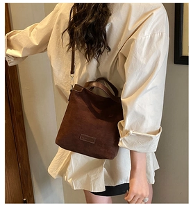 Détail d'un sac bandoulière en daim mat marron foncé avec crochets en métal et logo