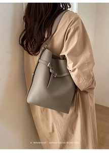 Minimalist taupe bucket bag with litchi texture shown on a khaki trench coat
