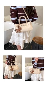 Close-up of cream leather shoulder bag with decorative strap and brown horse charm detail
