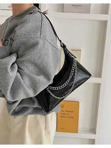 Detail of black glossy patent leather shoulder bag with decorative double silver chain