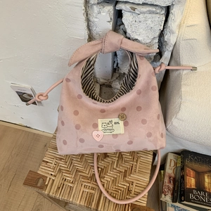 Detail of pink polka dot handbag with bow handle and cartoon patches on woven stool