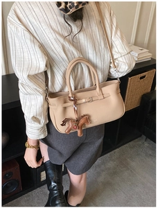 Detail view of beige lychee grain shoulder bag with a brown horse charm and metal buckle