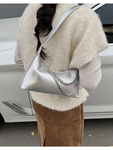 Detail of silver chain on metallic dumpling bag worn over shoulder in urban setting