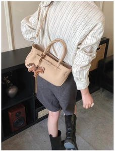 Detailed view of beige leather crossbody bag featuring strap buckle and horse pendant charm
