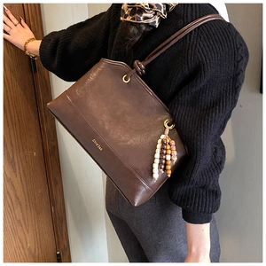 Detailed macro view of retro brown tote bag featuring beaded tassels and gold brand logo