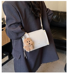 Detail of light gray crossbody bag with gold logo and brown plush doll accessory