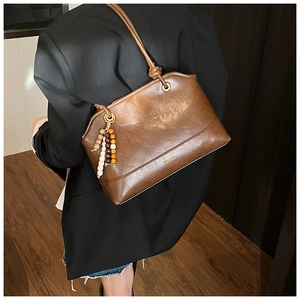 Detail view of brown vintage leather tote bag with wavy top and wood bead charm