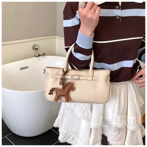 Detail of creamy white lychee grain handbag with buckle strap and brown horse charm