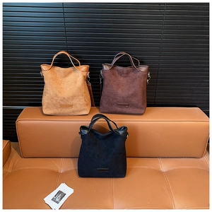 Trois sacs cabas minimalistes en daim marron, café et noir sur un banc en cuir