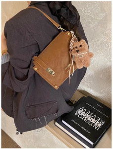 Detailed side view of brown suede handbag with gold clasp and plush dog charm accessory