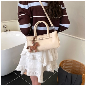 Detail of cream shoulder bag with horse charm and brand logo in a lifestyle setting