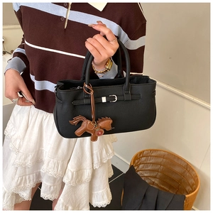 Detail of black leather handbag with horse charm accessory and stylish strap buckle design