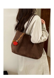 Detail of brown suede tote bag with colorful pom-poms and leather straps shown on shoulder