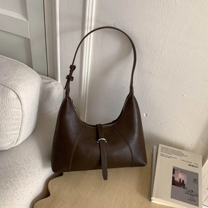Detail of a dark brown half-moon underarm bag featuring decorative metal ring and leather strap