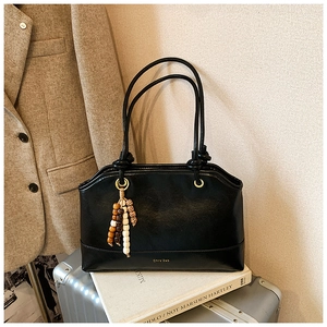 Close-up of black leather tote bag with brand logo and beaded tassel on a silver suitcase