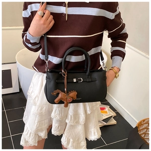 Detail of a black leather Boston-style handbag with horse charm and detachable strap