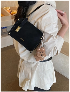 Detail of black matte leather square handbag with gold rotary lock and plush dog charm