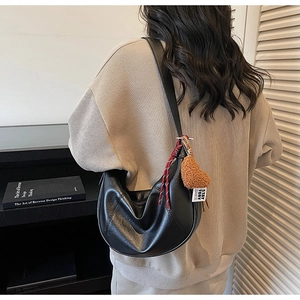 Detail of black crescent moon shoulder bag with cute bear charm and woven cord on leather strap