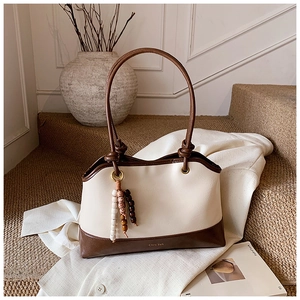 Detail of cream tote bag featuring wooden bead pendant and knotted handle design