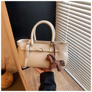 Detail of minimalist beige handbag with lychee leather texture and horse charm