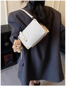 Detail view of beige crossbody bag with gold logo and cute plush puppy charm accessory