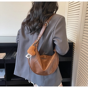 Minimalist brown crescent leather shoulder bag with plush heart charm on casual outfit