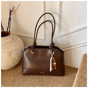 Detail of dark brown tote bag featuring metal rings and a boho beaded charm accessory