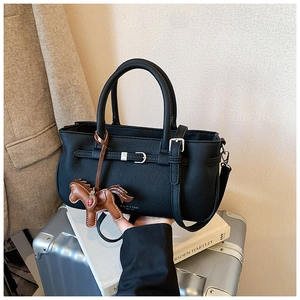 Detail of black lychee leather handbag with decorative horse charm on a silver suitcase