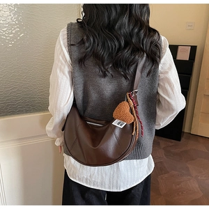 Detail of dark brown crescent bag with heart plush charm and braided cord on model