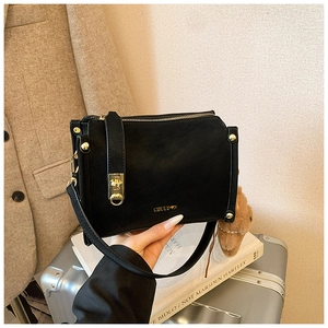 Close-up of black leather handbag with gold hardware, brand lettering and brown bear charm