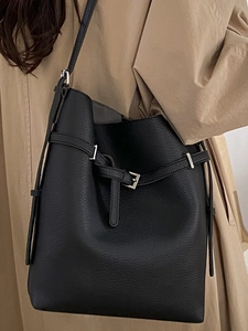 Chic black lychee leather bucket bag with silver buckle worn with a trench coat