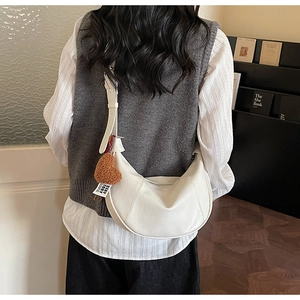 Detail of white crescent bag with heart charm and stitched faux leather texture
