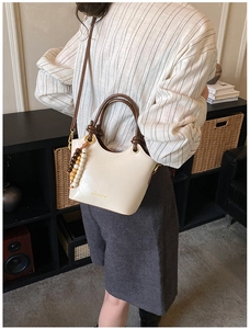 Détail d'un sac seau beige avec poignées marron et perles en bois sur un mannequin