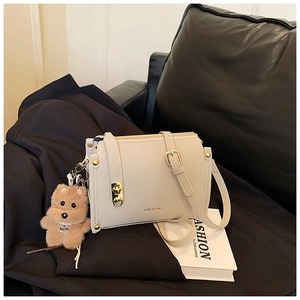Detail of off-white leather handbag with gold logo and plush dog charm on sofa