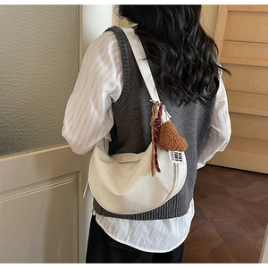 Detail of white moon-shaped hobo bag featuring a plush heart charm and textured finish