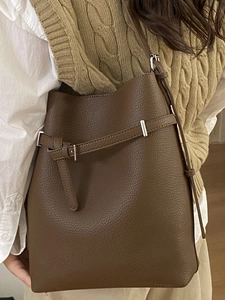 Brown lychee leather bucket bag with silver buckle worn by a woman over a beige vest